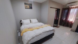 A bedroom with a bed, white walls, a painting, and a window with curtains.