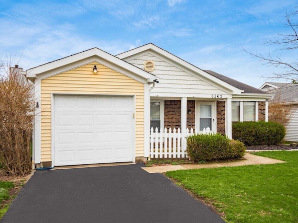 Une maison de plain-pied avec un garage, une véranda et un petit jardin devant.