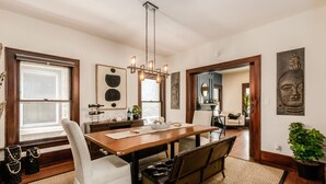 Un comedor con mesa de madera, sillas tapizadas de blanco, una araña y obras de arte en las paredes.