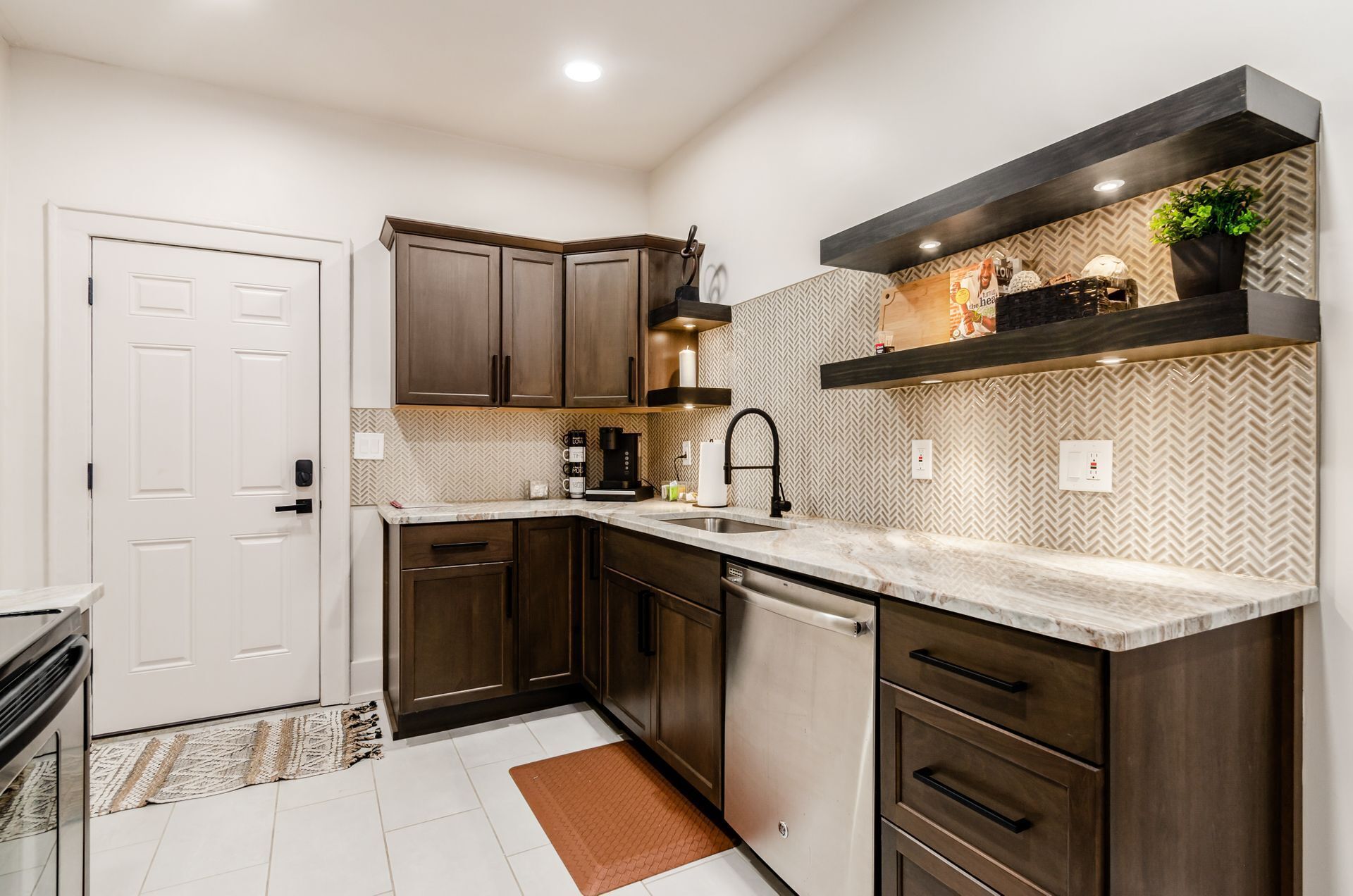 A compact kitchen with dark wooden cabinets, a stainless steel dishwasher, and a marble countertop.