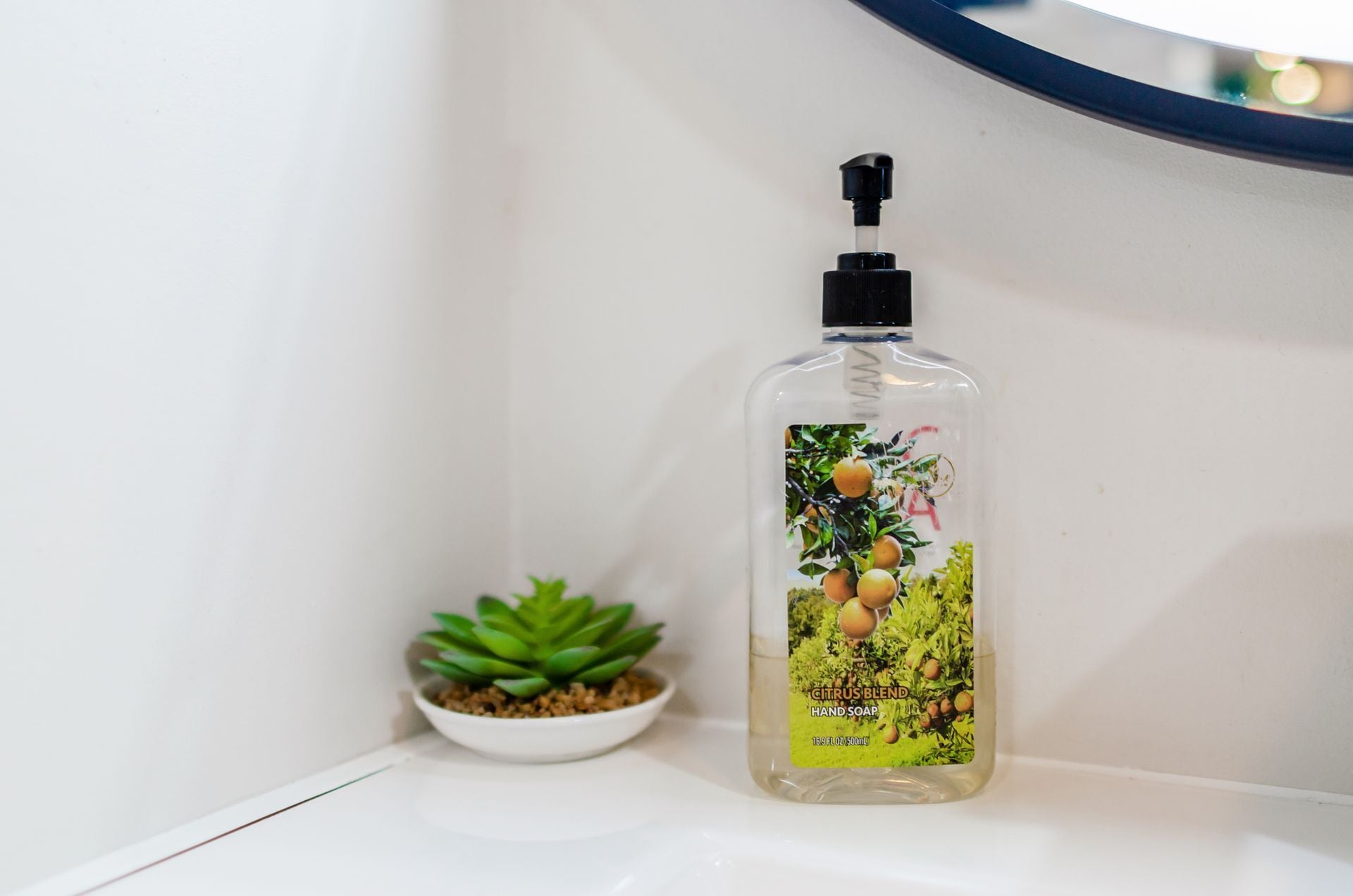 Una botella de jabón de manos con aroma cítrico sobre una estantería blanca, junto a una pequeña planta en maceta.