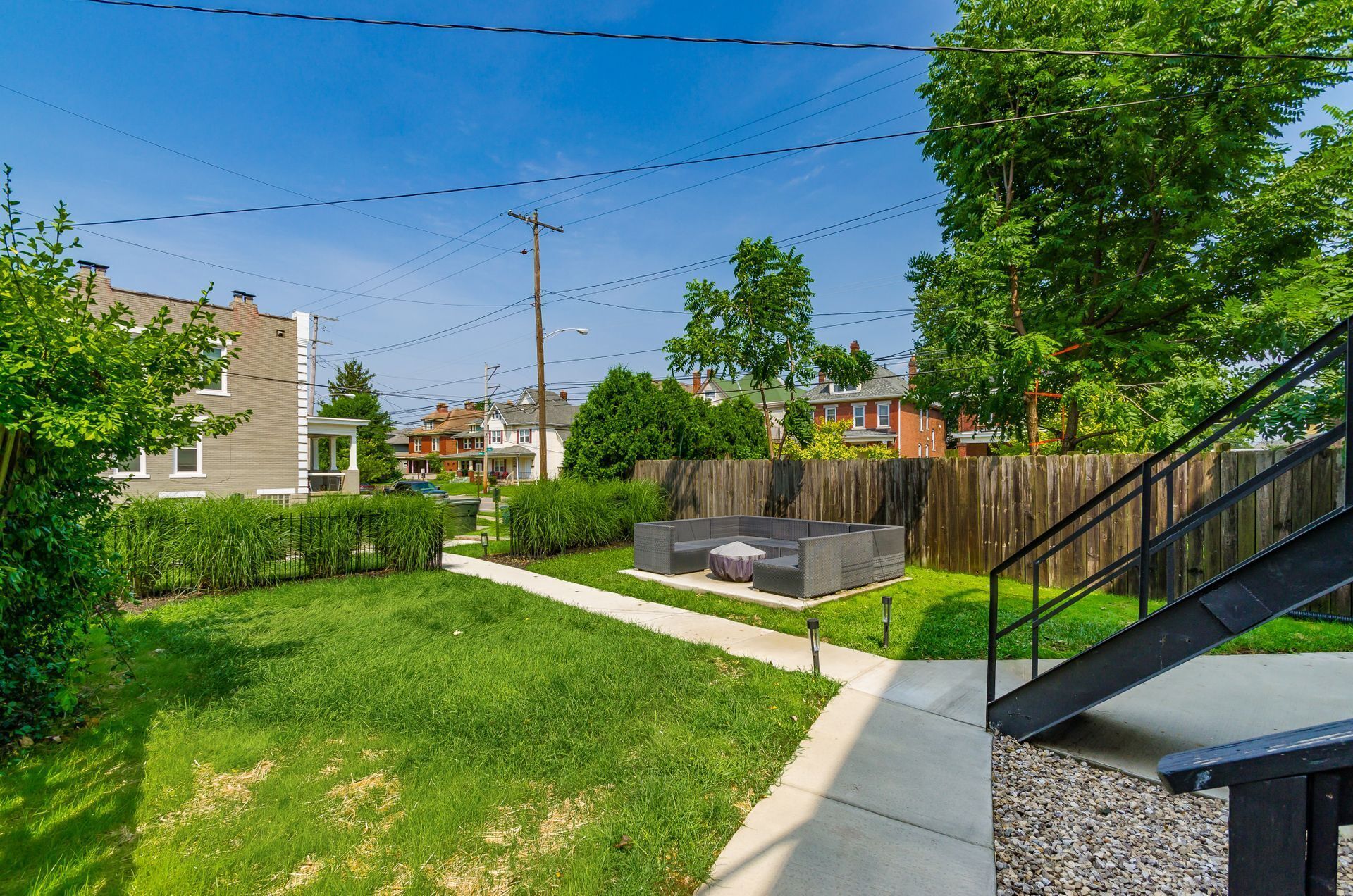 A residential backyard with a paved patio, a wooden fence, and a grassy lawn.