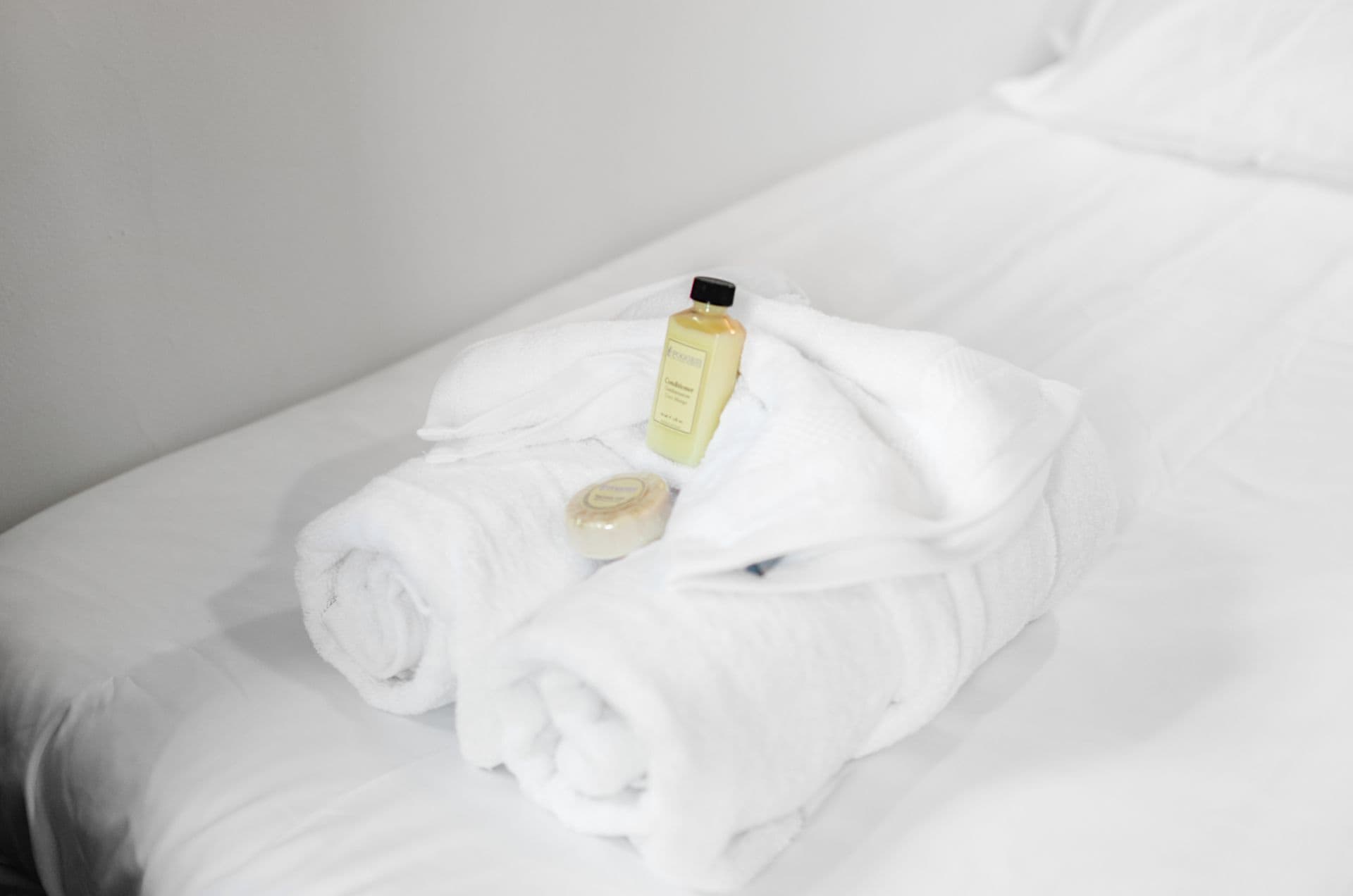 A neatly folded white towel on a bed with a bottle of lotion and a bar of soap.