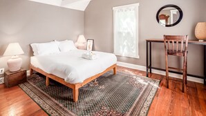 A bedroom with a wooden bed, a desk with a chair, a window with curtains, and a chandelier.