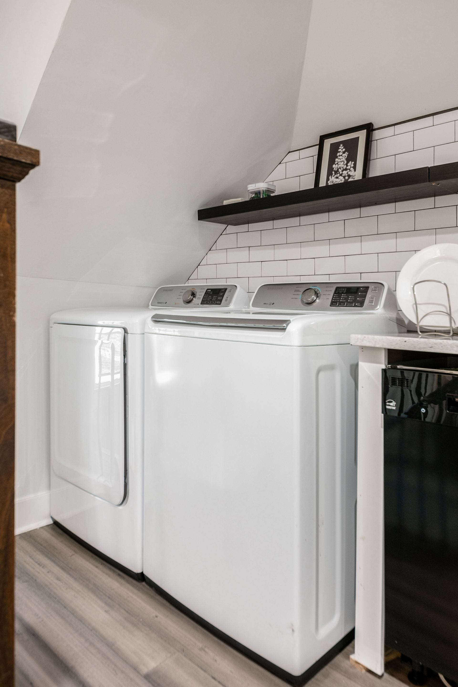 Een wasruimte met een voorlader wasmachine en droger, een houten kast en een betegelde spatwand.