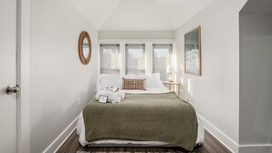 A bedroom with a bed, a bedside table, a mirror, and a window with blinds. - Columbus Getaway! Stylish Apartment! (Columbus)