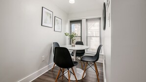 A dining area with a round table, four chairs, a vase with a plant, and framed pictures on the wall. - Columbus Getaway! Stylish Apartment! (Columbus)