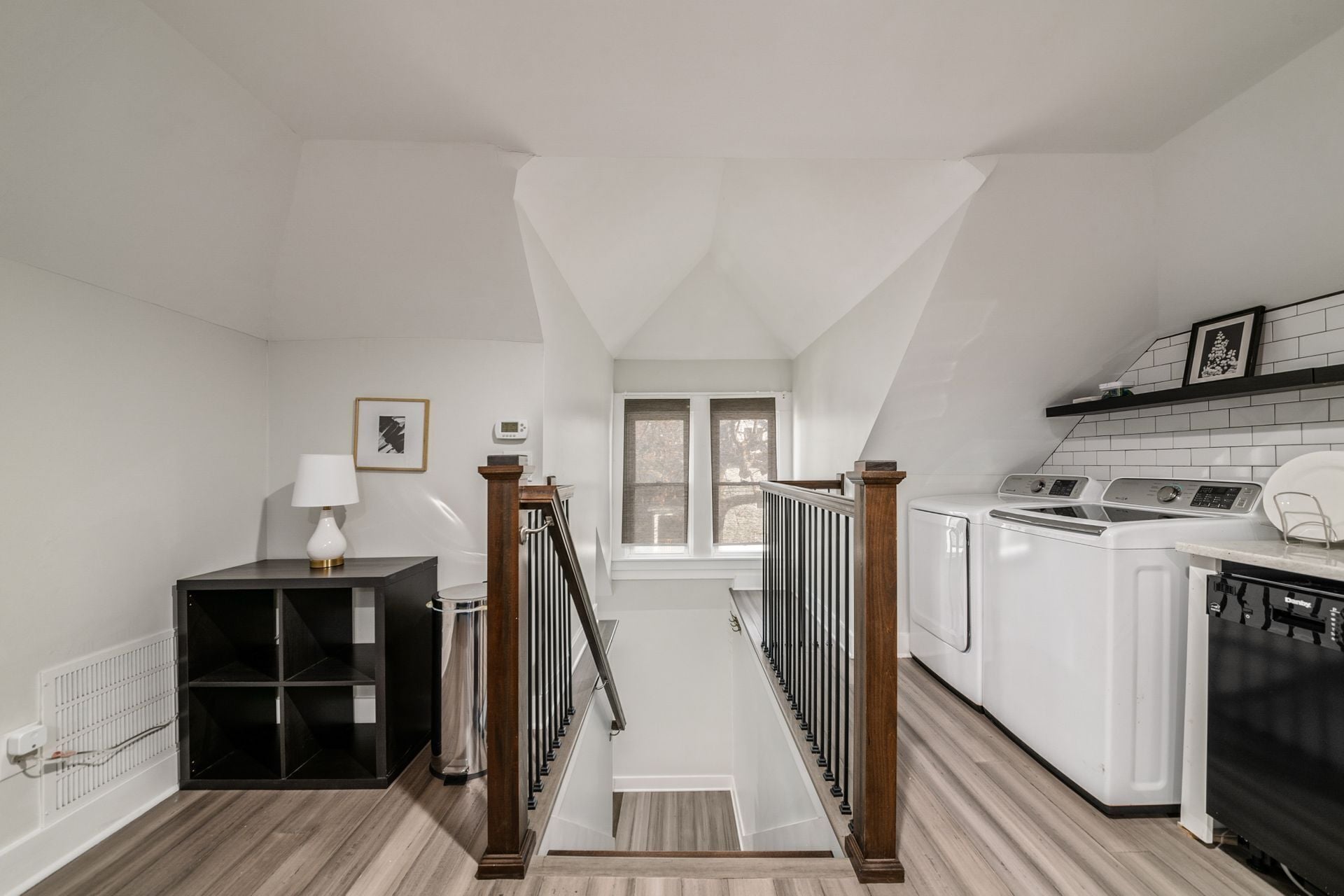 A modern kitchen with a built-in washer and dryer, a wooden staircase, and a view to the outside.