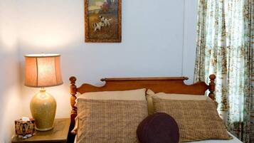 A bedroom with a wooden bed, two pillows, a round pillow, a lamp, a painting, and floral curtains.
