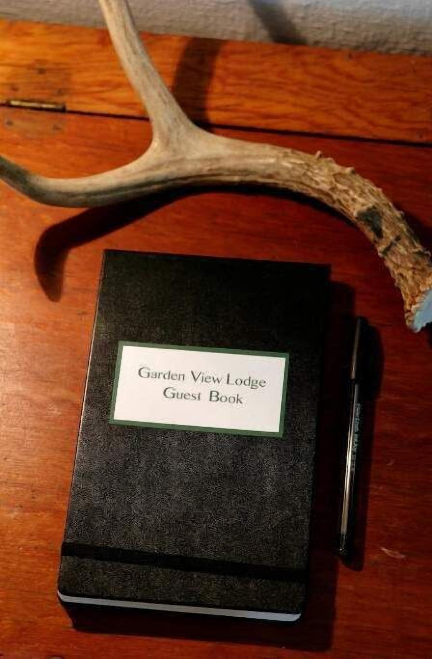 Un livre d’or noir intitulé « Livre d’or du Garden View Lodge » est posé sur une table en bois, à côté d’une branche de cerf.