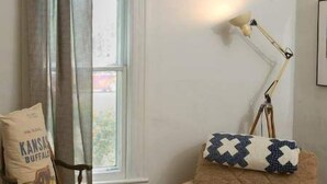 A cozy room with a brown armchair, a wooden chair, a lamp, and a window with curtains. - Garden View Lodge (Lucas)
