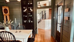 A dining area with a white table and black chairs, wooden flooring, and a dark green wall with a built-in cabinet.