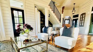 A spacious living room with a glass coffee table, white sofas, and a patterned rug.