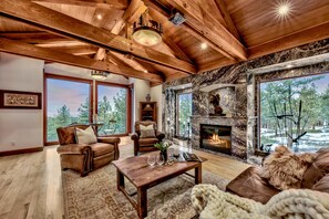 A spacious living room with a fireplace, leather furniture, and large windows offering a view of the outdoors. - Luxe10 Bear Claw Estate Lakeview W Pool (Zephyr Cove)