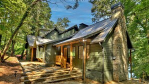 Un chalet rustique avec une cheminée en pierre, une véranda en bois et un sentier de terre menant à l’entrée.