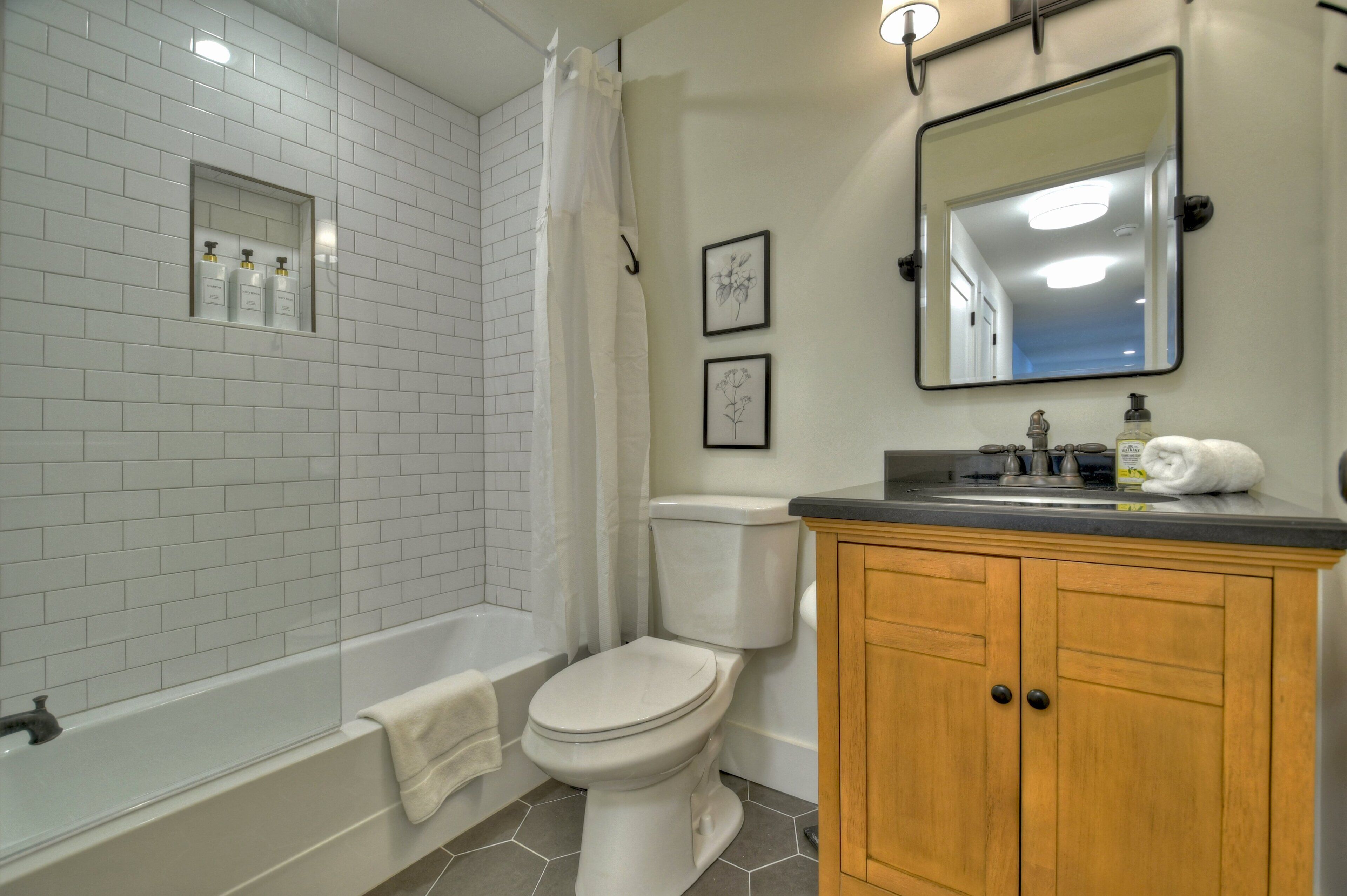 A bathroom with white tiled walls, a bathtub, a toilet, a wooden vanity, and a mirror.