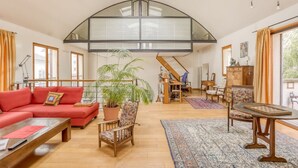 A spacious living room with a red sofa, wooden chairs, a coffee table, and a large potted plant. A staircase leads to an upper level with a glass railing. - Appartement Dombasle, Tour Eiffel - 3 étoiles - Welkeys (Paris)