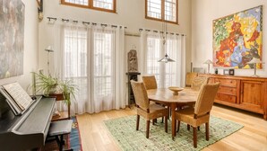 A dining area with a piano, wicker chairs, a wooden table, and a painting on the wall. - Appartement Dombasle, Tour Eiffel - 3 étoiles - Welkeys (Paris)