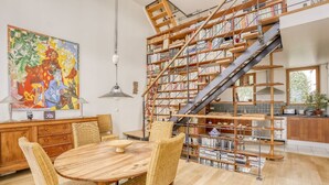 A dining area with a round wooden table and wicker chairs, a bookshelf with a staircase, and a large abstract painting on the wall. - Appartement Dombasle, Tour Eiffel - 3 étoiles - Welkeys (Paris)