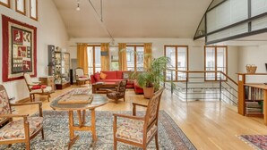 A spacious living room with a high ceiling, large windows, a red sofa, wooden furniture, and a staircase. - Appartement Dombasle, Tour Eiffel - 3 étoiles - Welkeys (Paris)