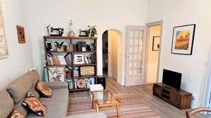 Ein Wohnzimmer mit einer Couch, einem Bücherregal, einem Fernseher und einem gemusterten Teppich.
