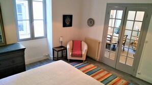 Ein Schlafzimmer mit einem Bett, einem Sessel, einem Heizkörper, einem Fenster und einer Tür, die auf einen Balkon führt.