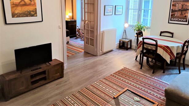 Ein Wohnzimmer mit Fernseher, einem Esstisch mit Stühlen, einem Kamin und einem Flur, der zu einem anderen Raum führt.