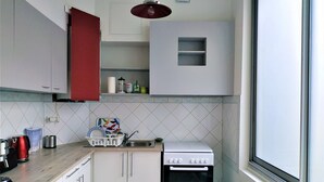 Eine kleine Küche mit weißen Schränken, einem roten Schrank, einer Spüle, einem Herd und einem Fenster mit Blick.