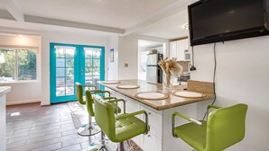 Una cocina moderna con una isla grande, taburetes de bar verdes, un televisor de pantalla plana y una puerta color turquesa.