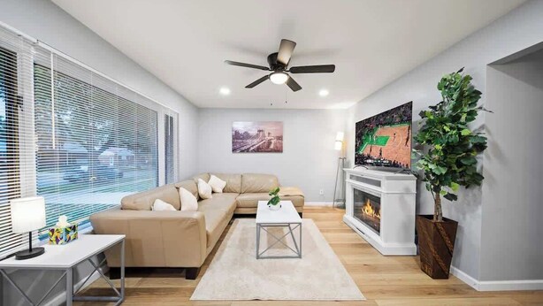 Un soggiorno moderno con un divano beige, un tavolino da caffè bianco, un caminetto e una ventola a soffitto.