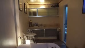 A small, dimly lit room with a bed, a small table, and a chair. There is a window with a view of the outside. - TerisitaPlace - Love At First (Taytay)
