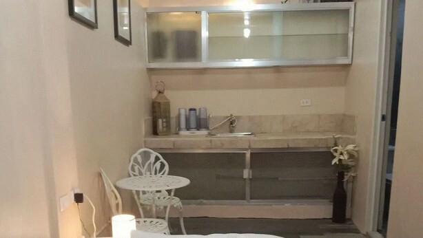 A small, neatly arranged room with a bed, a small table with chairs, a sink, and a mirror above the counter. - TerisitaPlace - Love At First (Taytay)