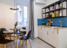 Una cucina moderna con zona pranzo, che presenta un tavolo rotondo con sedie, una mensola a incasso con utensili da cucina e una finestra con tende.