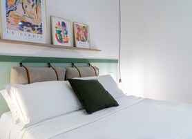 Un letto con cuscini bianchi e verdi, una testiera verde e due opere d'arte incorniciate sopra.
