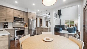 Une cuisine moderne équipée d’appareils électroménagers en acier inoxydable, un coin repas avec une table ronde et un espace de vie comprenant un canapé et un escalier.