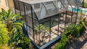 A modern house with a large glass conservatory, a swimming pool, and lush greenery. - Theater Room | Kids Bunk Bedroom | Screened in Private Pool (Kissimmee)