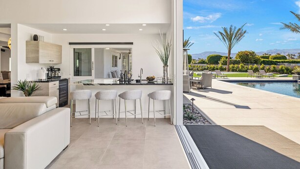 Cozinha moderna com área de bar, espaço para sentar junto à piscina e vista para um jardim ajardinado.