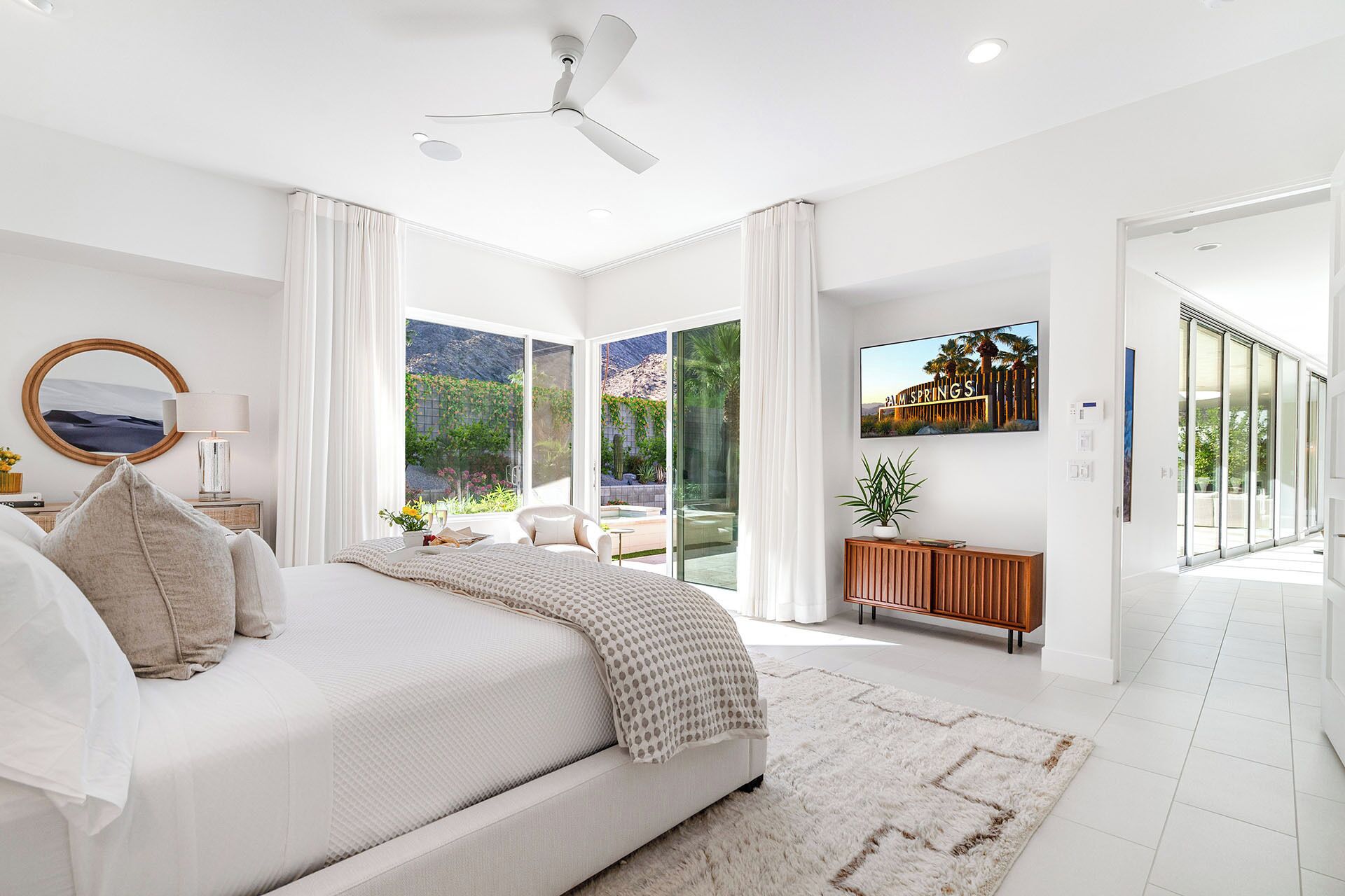 Un dormitorio moderno con una cama grande, un ventilador de techo y vistas a un jardín a través de puertas de vidrio.