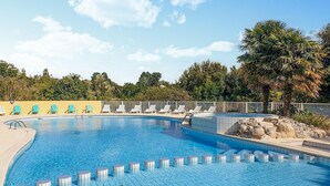 En swimmingpool med kristallklart blått vatten, omgiven av solstolar och en palm.