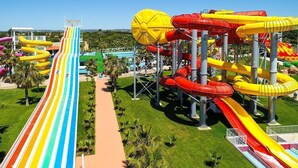 A water park with multiple slides and pools, surrounded by greenery and a clear sky.