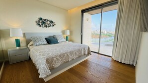 A bedroom with a large bed, a nightstand, a lamp, and a view of the outside through a sliding glass door.