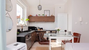 A modern kitchen with a dining area, featuring a white refrigerator, wooden cabinets, and a glass dining table. - house 5 miles to an Old Town with double walk-in shower and Victorian tub (Borkowo)