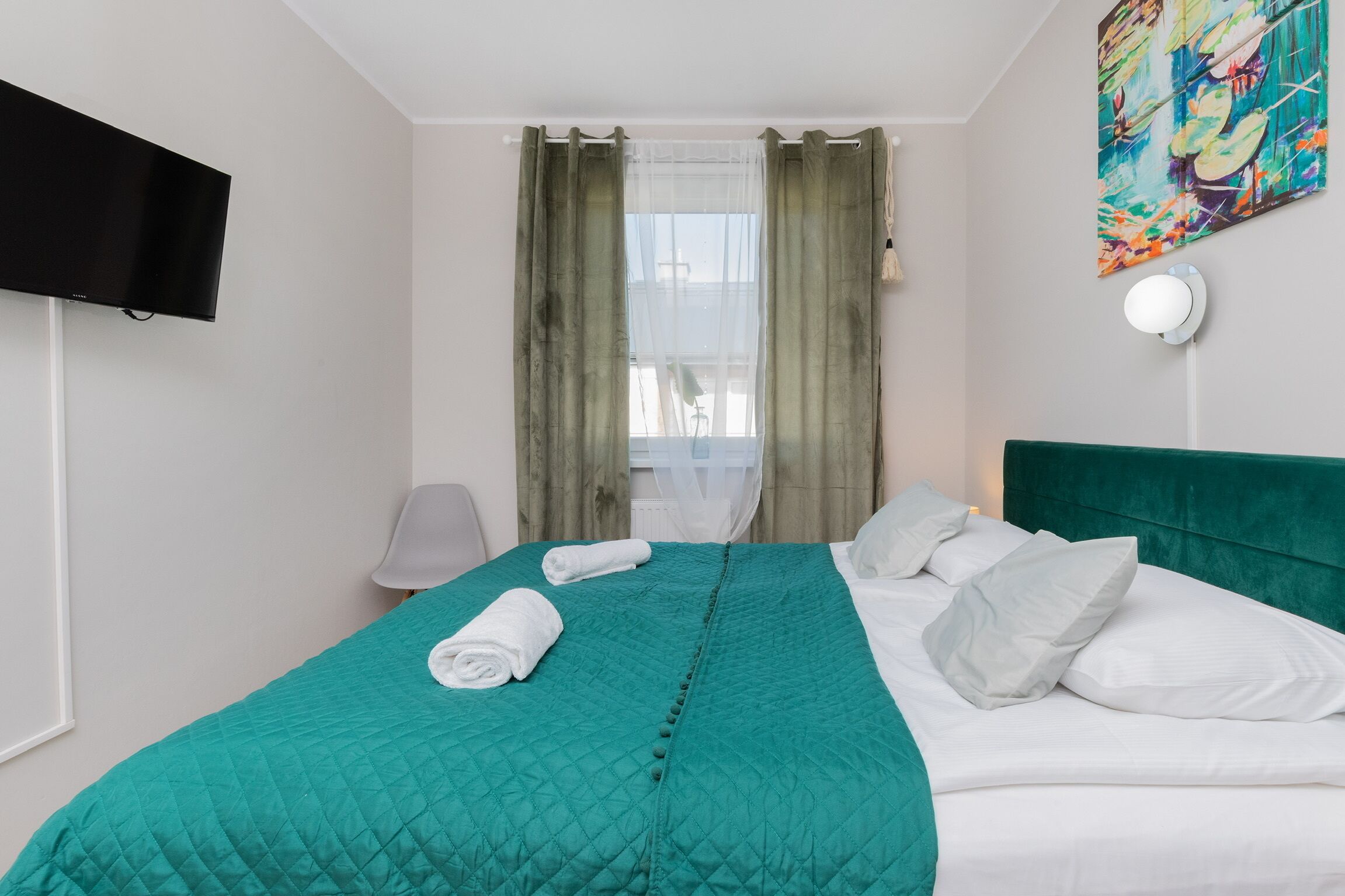 Habitació d'hotel amb un llit, una televisió, una cadira i un quadre al mur.