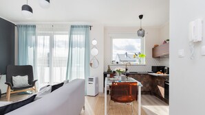 A modern living room with a sofa, a chair, and a dining table with chairs. There is a kitchen area with a window, a hanging light, and a phone on the wall. - house 5 miles to an Old Town with double walk-in shower and Victorian tub (Borkowo)