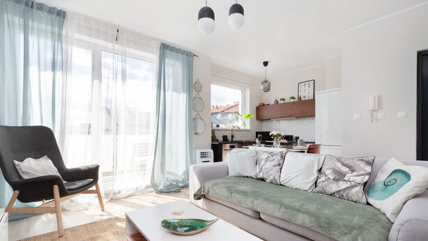 A modern living room with a sofa, armchair, and coffee table. There is a kitchen area in the background with a window overlooking the city. - house 5 miles to an Old Town with double walk-in shower and Victorian tub (Borkowo)
