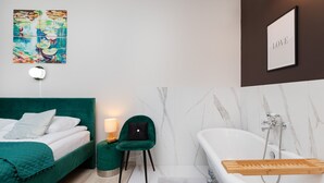 A modern bathroom with a white bathtub, a green chair, and a bedside table with a lamp. - house 5 miles to an Old Town with double walk-in shower and Victorian tub (Borkowo)