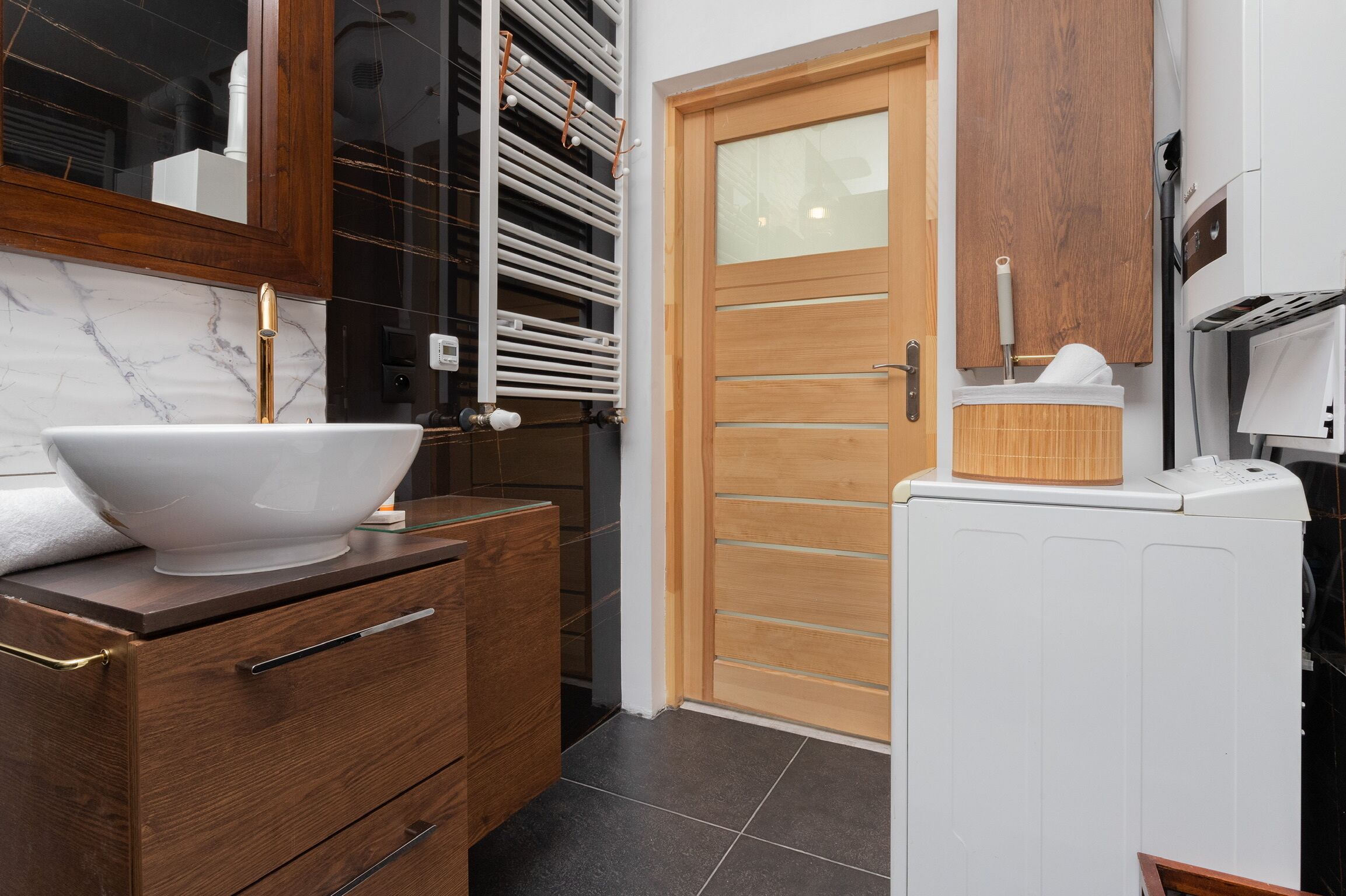A modern bathroom with a large white sink, wooden cabinetry, and a white washing machine.