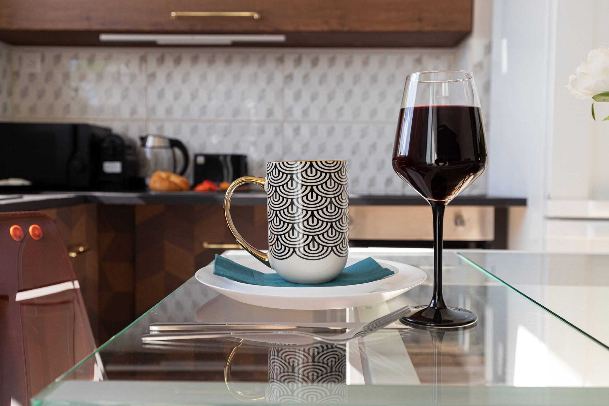 A glass table with a white mug and a wine glass.