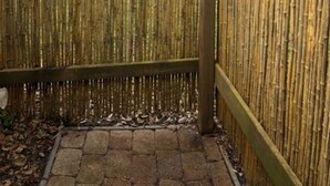 Een bamboomschutting met een houten paal en een metalen poort.