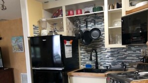 Een keuken met een zwarte koelkast, een fornuis en een spoelbak. Boven het aanrecht zijn kastjes en een betegelde spatwand.